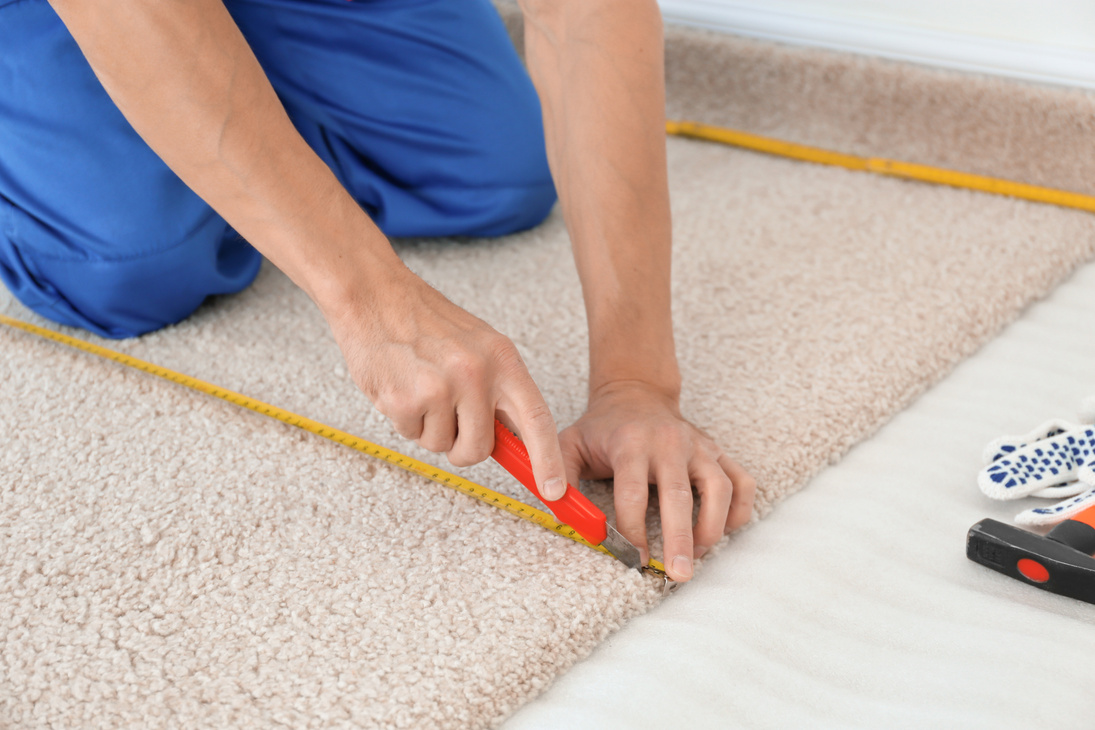 Worker Using Cutter While Installing New Carpet Flooring in Room
